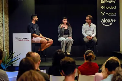 The panel on stage seen past the audience, partner logos on the wall.