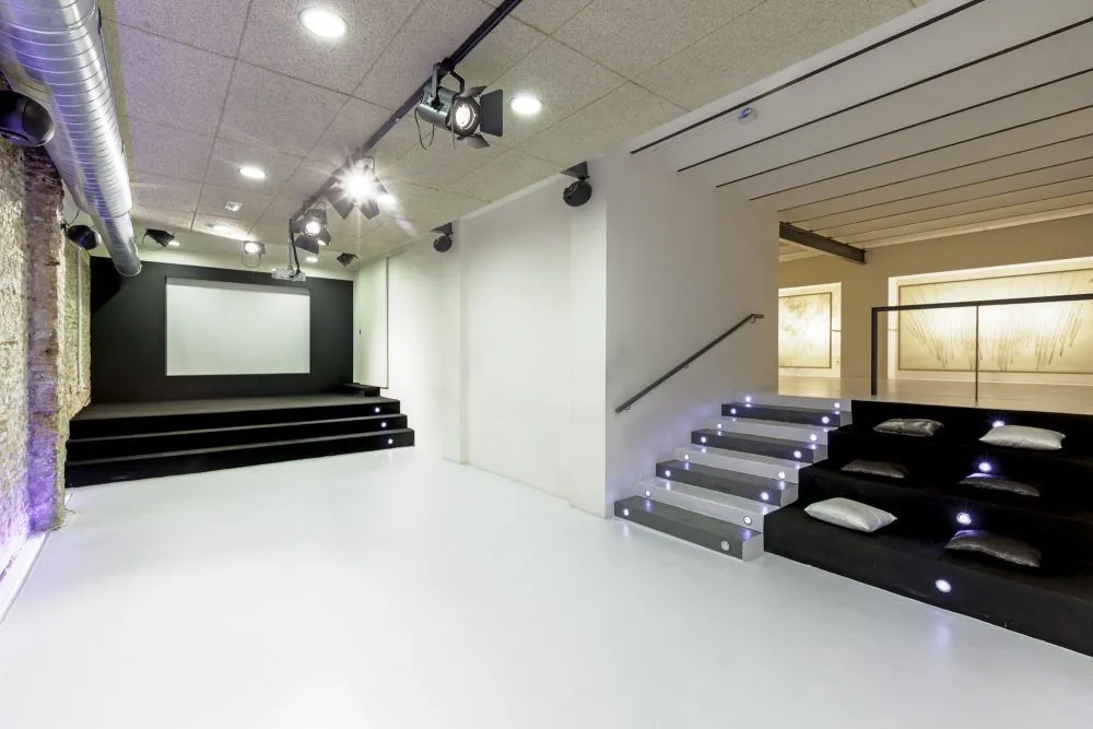 Auditorium with a stage, projection screen and tiered seating steps.
